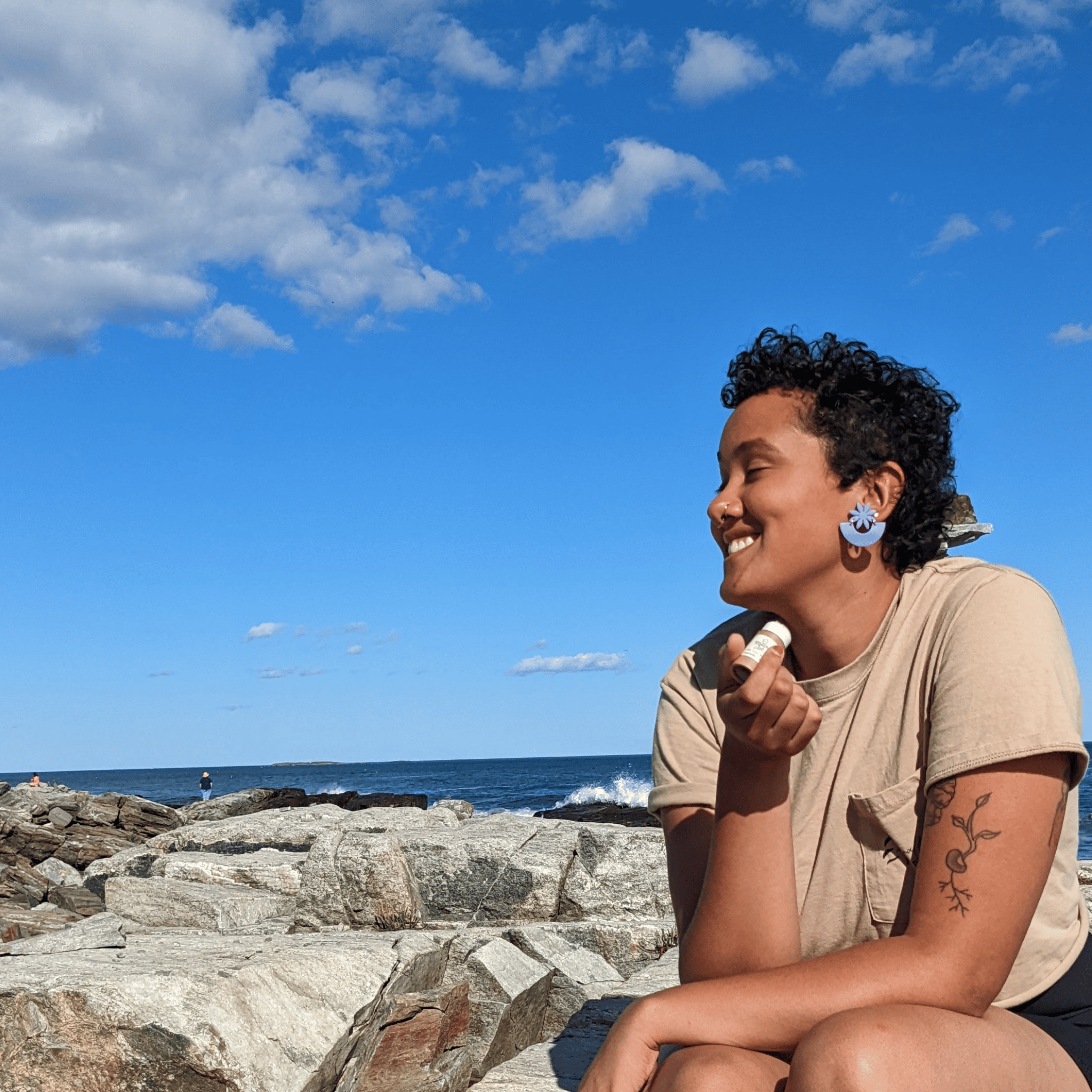 Person holding Mellow Oak CBD lip balm on rocks by the ocean