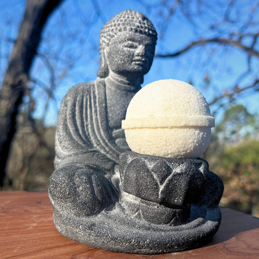 A white bath bomb sitting on a lotus flower in buddha's lap