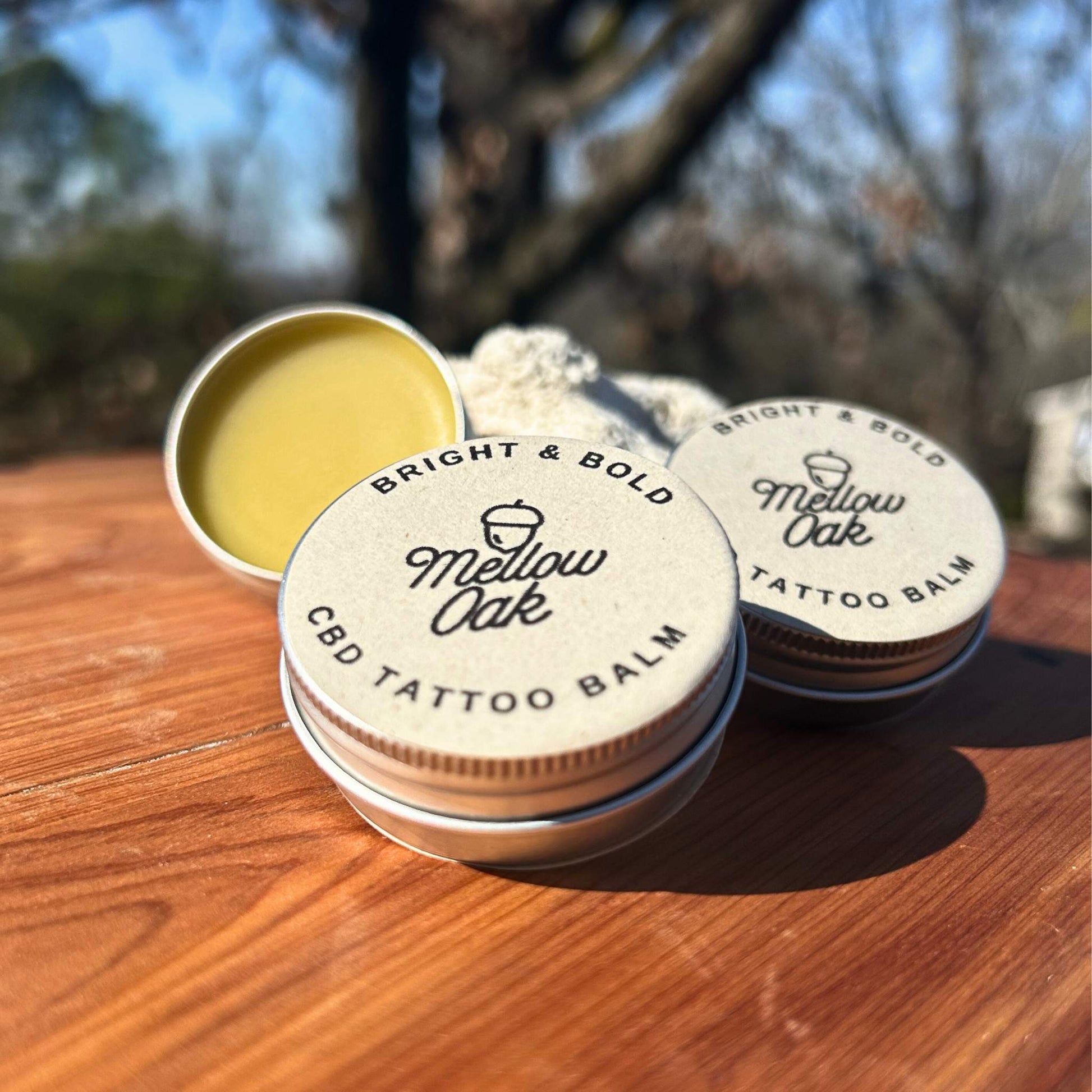 CBD tattoo balm outside on some wood underneath some trees