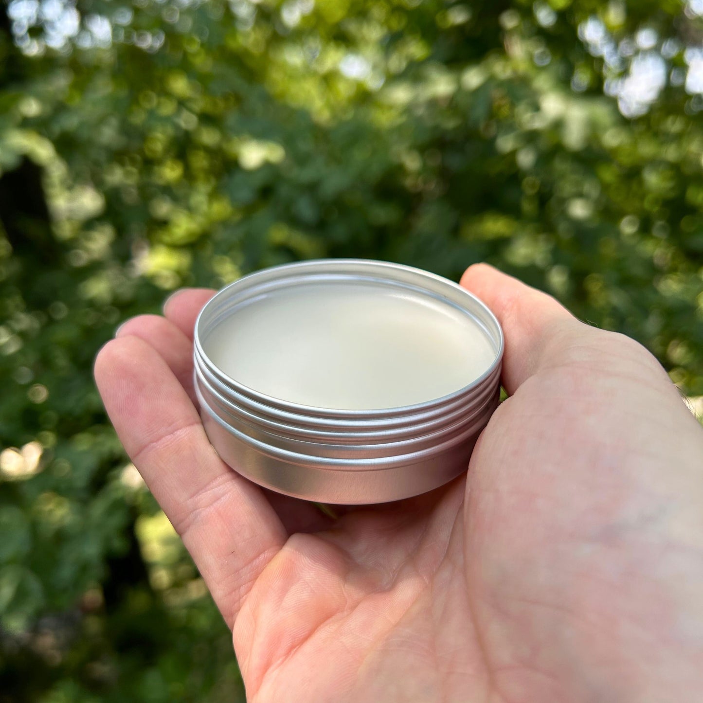 man holding a tin of cbd muscle salve with trees in the background