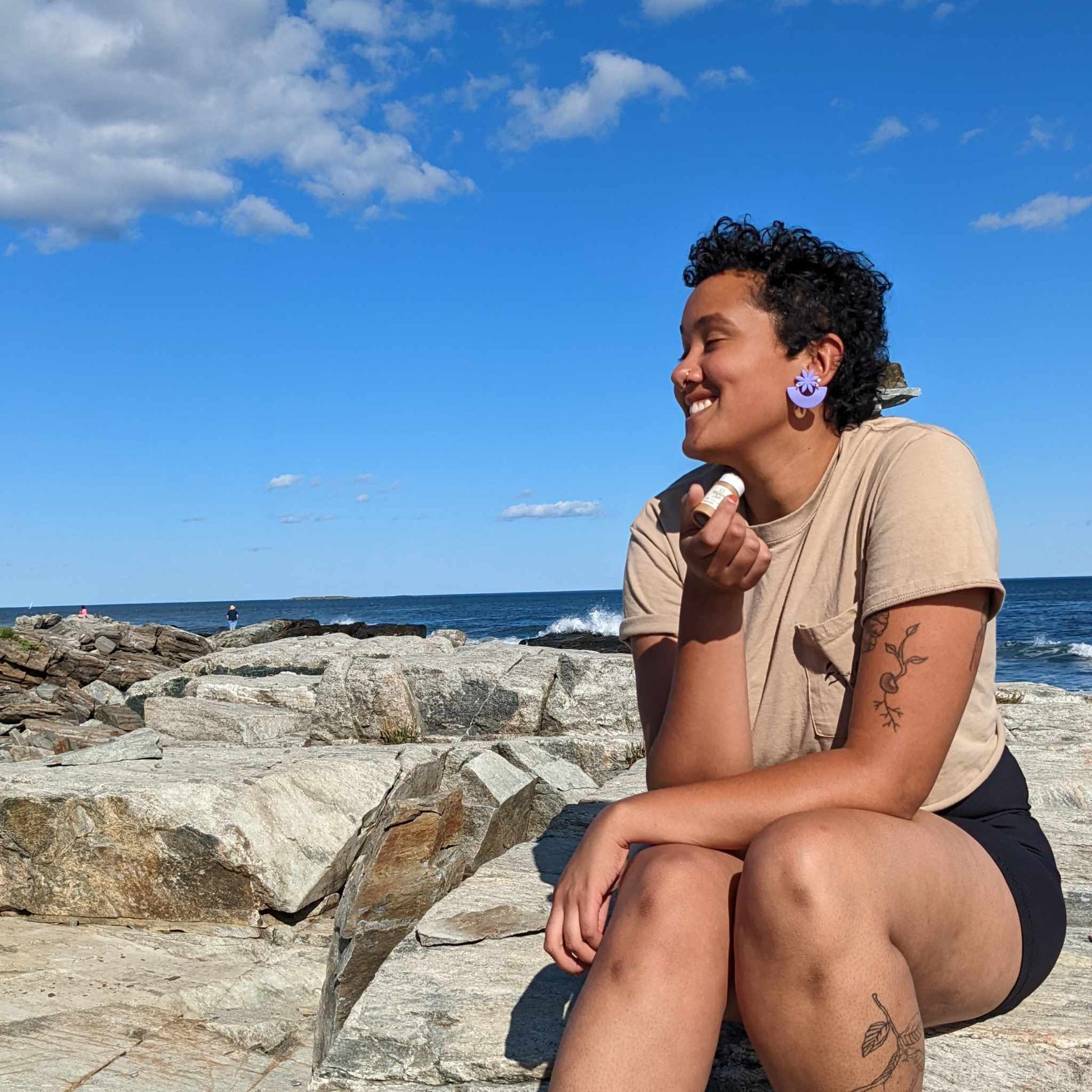 Smiling woman by the ocean holding a cbd lip balm