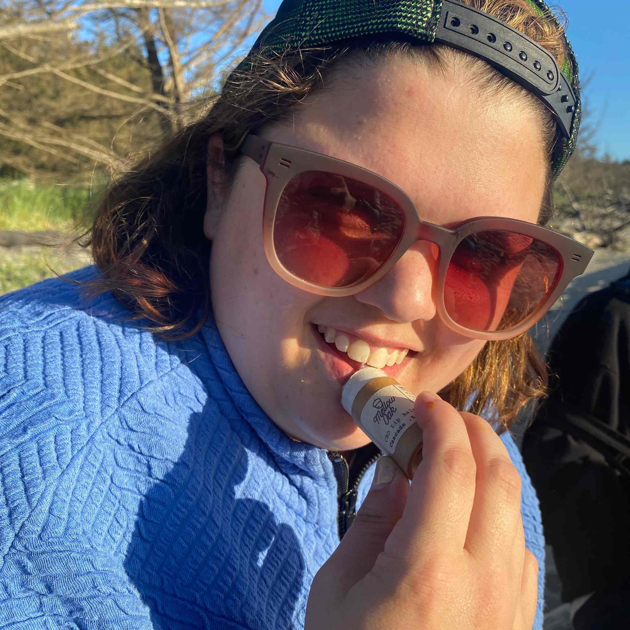 Woman applying cbd lip balm packaged in eco-friendly packaging to her lips outside