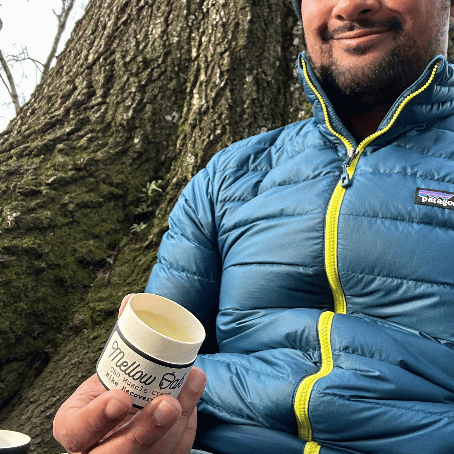 Man holding cbd muscle salve next to a tree